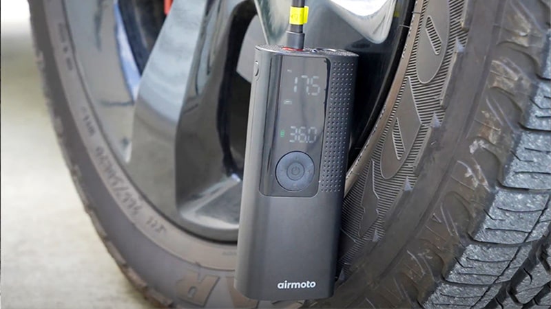 Airmoto tire inflator attached to a car tire showing live pressure on its digital gauge