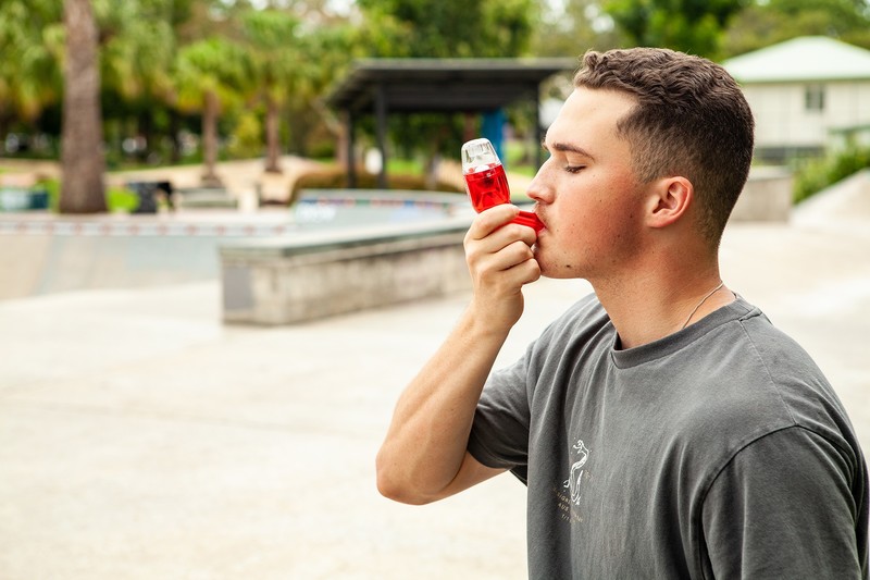 Young man using the red AirPhysio Sports OPEP device outdoors at a skate park