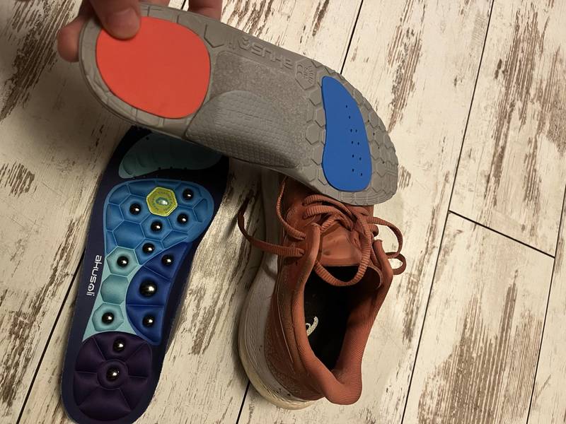 Akusoli insole showing the acupressure node top surface and cushioned underside next to a running shoe