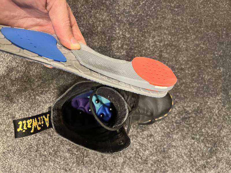 Akusoli magnetic acupressure insole held above a boot, showing its grey underside and red heel pad
