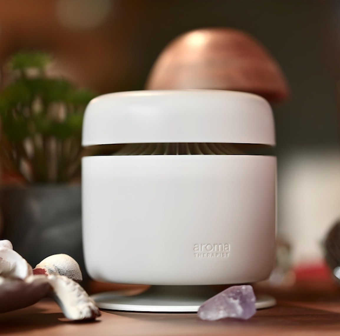 Aroma Amplifier waterless diffuser on a tabletop beside a lamp and plant