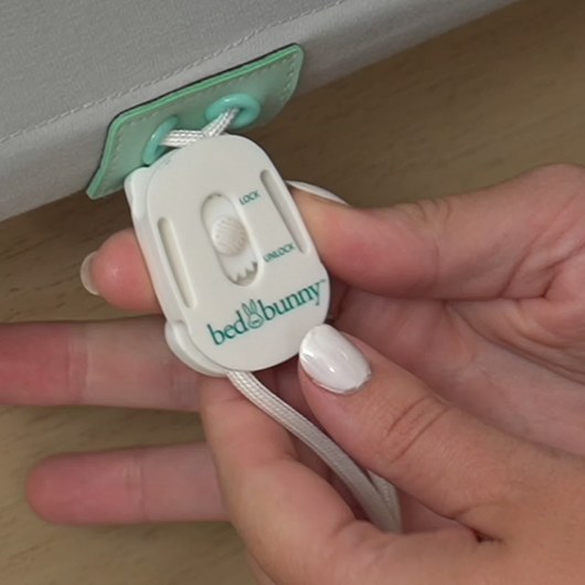 Hands holding the white Bed Bunny locking clip with its LOCK and UNLOCK slider