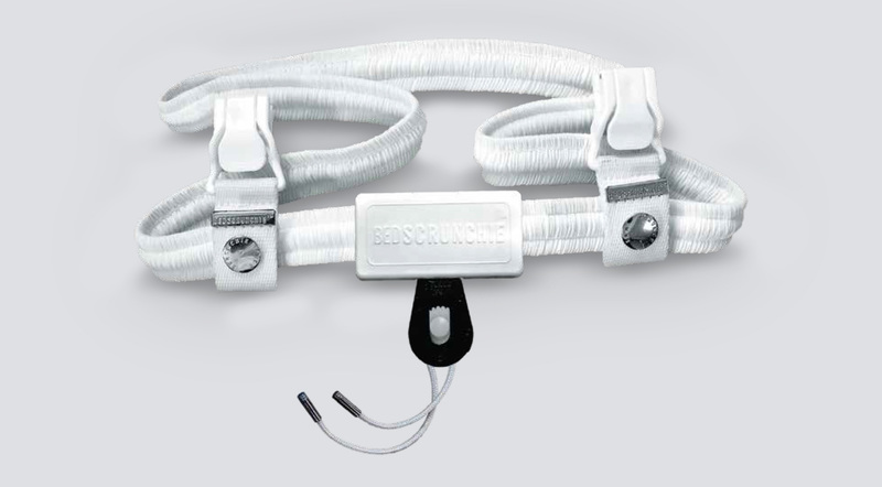 The Bed Scrunchie sheet fastener, an elastic band with eight clips and a central drawcord, laid out on white