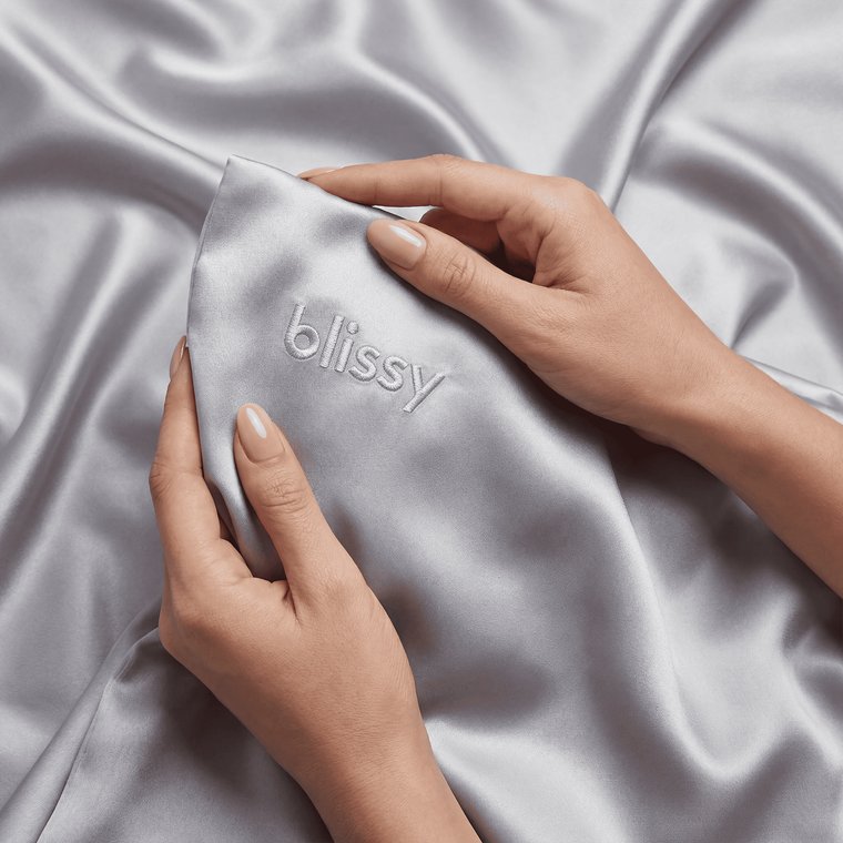 Hands running over the smooth silver Blissy mulberry silk pillowcase fabric