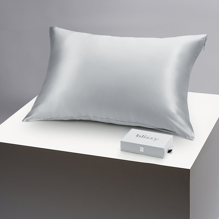 The silver Blissy silk pillowcase on a pedestal beside its gift box