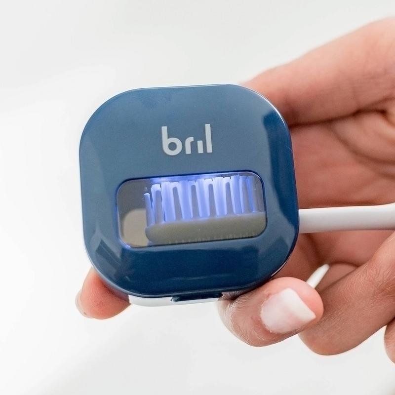 Hand holding the Bril UV toothbrush sanitizer with its UV-C light glowing inside