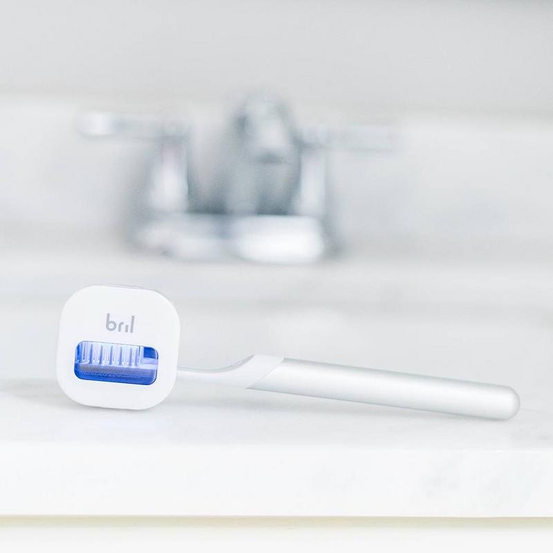Bril UV toothbrush sanitizer clipped over a manual toothbrush head on a bathroom counter