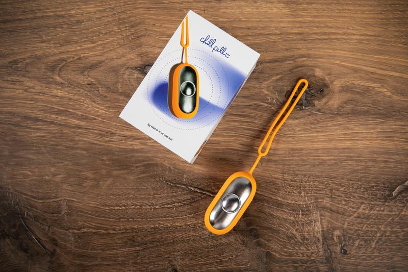 The Chill Pill calm device next to its retail packaging box on a wooden surface