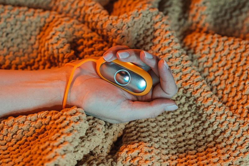 The Chill Pill calm device lit up and resting in a hand on a cozy knit blanket