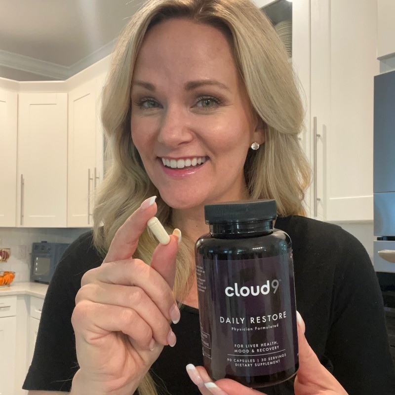 Person in a kitchen holding a Cloud 9 Daily Restore bottle and an open capsule