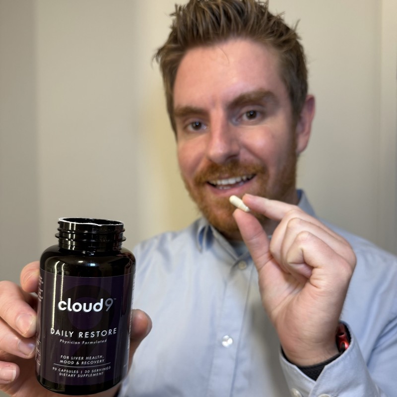 Person holding a Cloud 9 Daily Restore bottle and capsule indoors