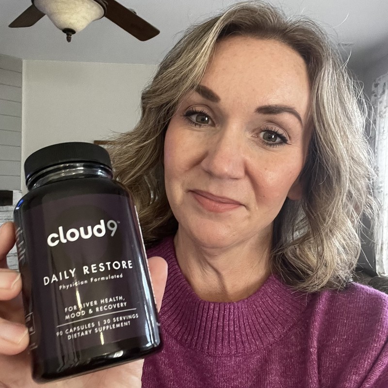 Person holding a Cloud 9 Daily Restore bottle in a home setting