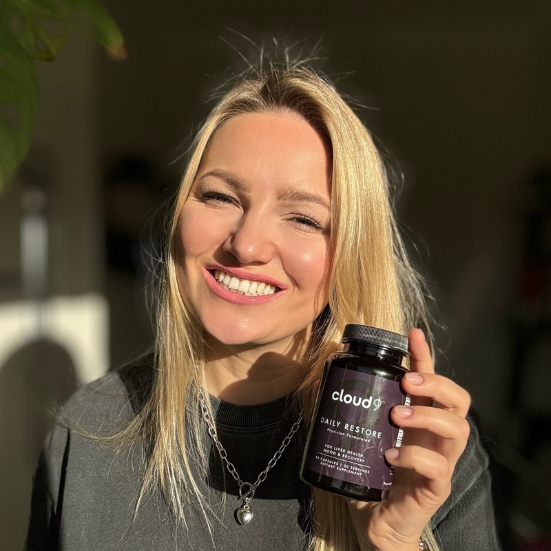 Person holding a Cloud 9 Daily Restore bottle outdoors in natural light