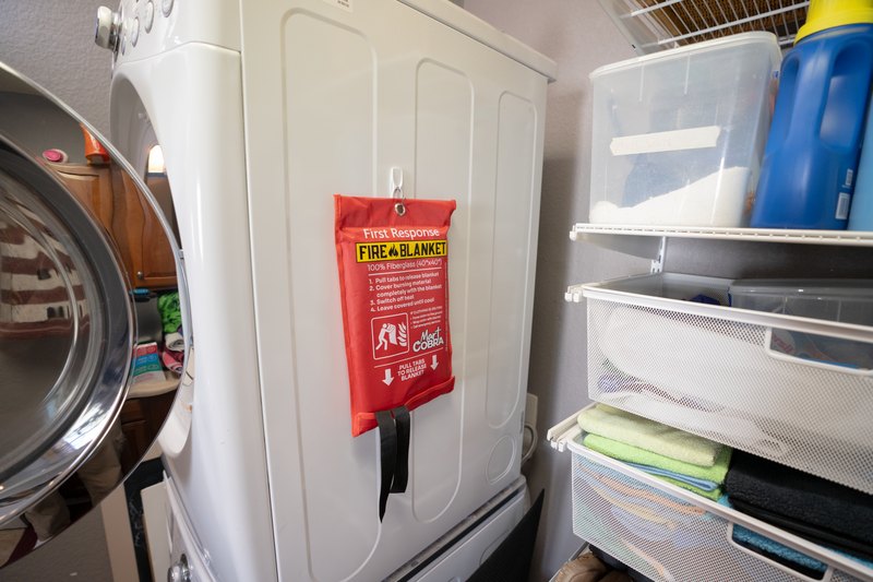 Cobra fire blanket pouch mounted on a laundry-room dryer next to shelving