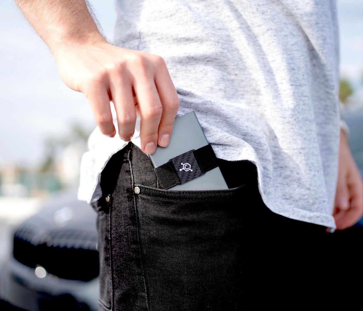 A person sliding the Code 118 aluminum wallet into the back pocket of black jeans