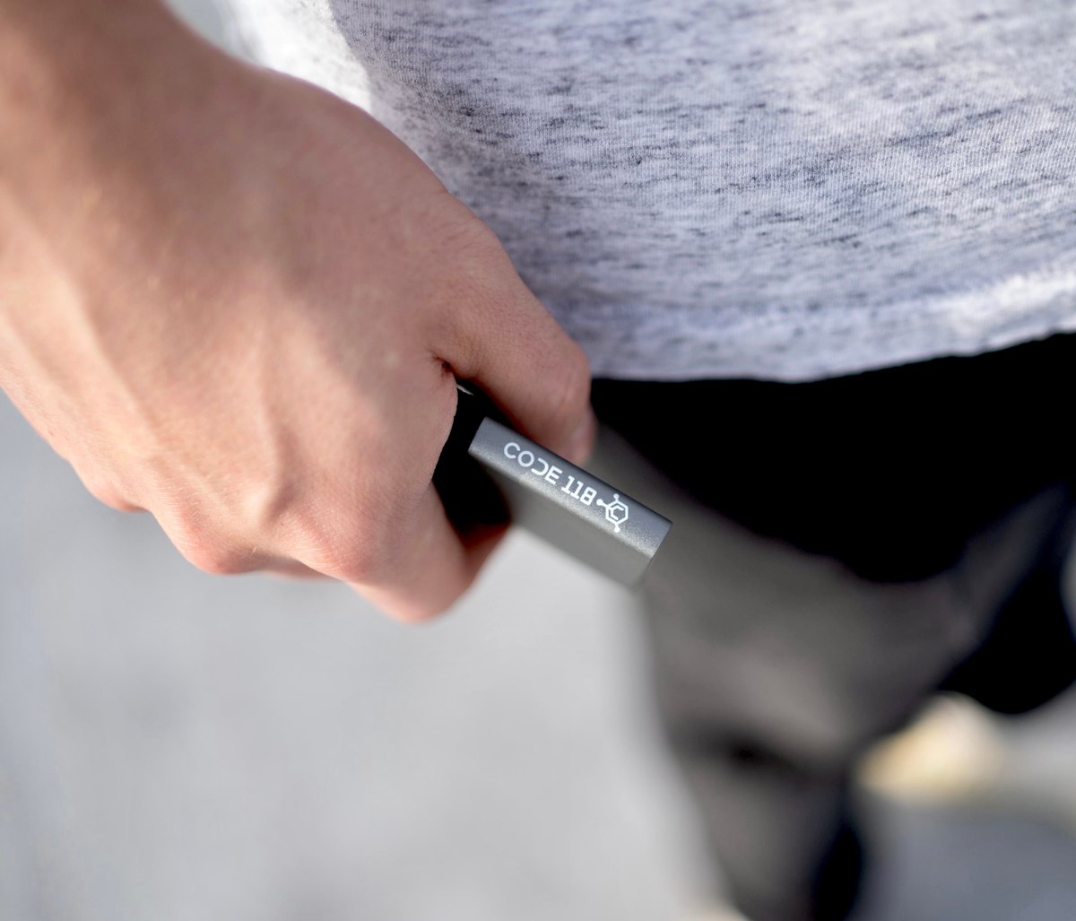 Close-up of the slim Code 118 aluminum wallet held between fingers showing the engraved logo and quarter-inch profile
