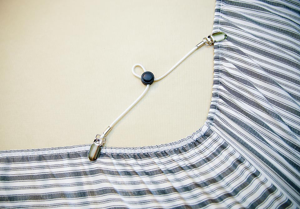 The Original Bed Band corner strap with an elastic cord, metal clamps and a cord-lock on a mattress corner