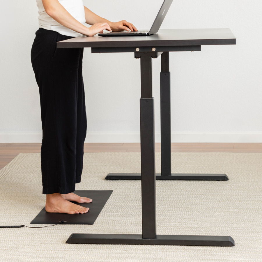 Person standing barefoot on the Earthing Universal Mat at a standing desk