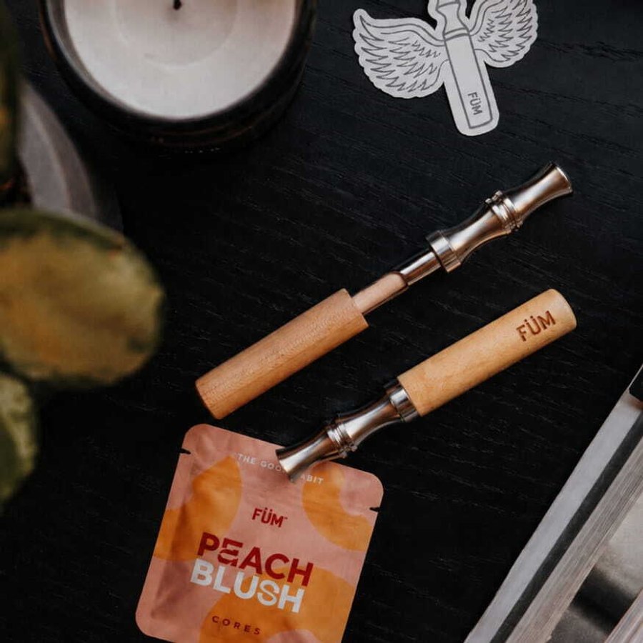 Two FÜM wooden flavored-air devices with steel mouthpieces beside a flavor core pack