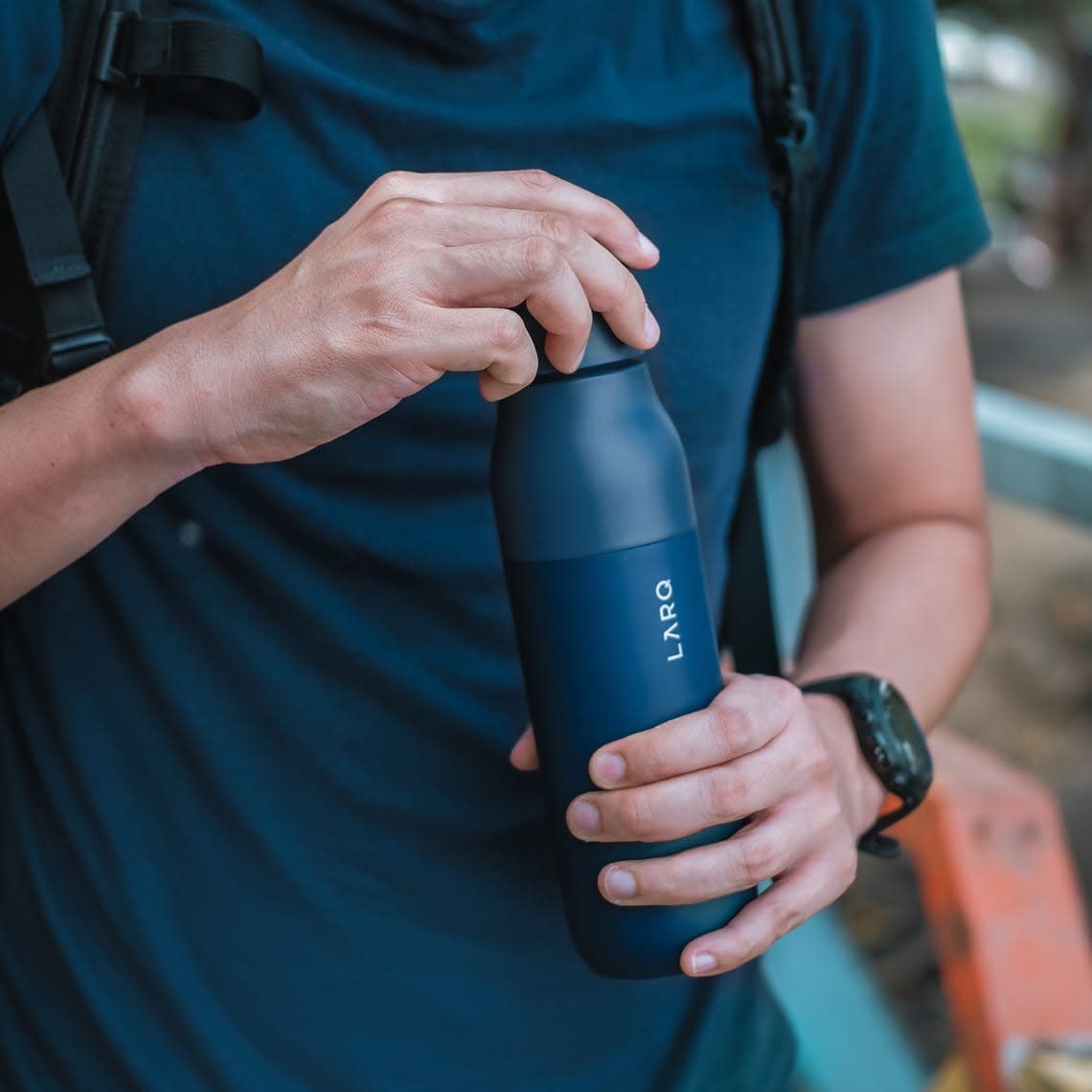 A person holding the navy LARQ Bottle PureVis self-cleaning water bottle outdoors