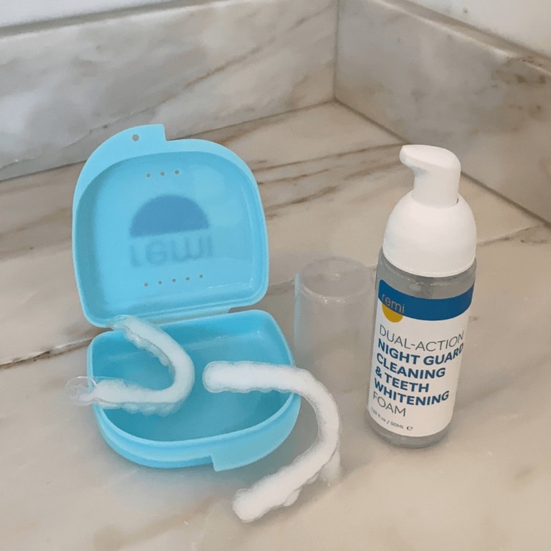 Remi Night Guard Cleaning and Teeth Whitening Foam bottle beside a night guard in its blue case on a marble counter