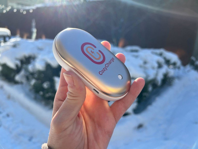 A hand holding the CozyCharge rechargeable hand warmer outdoors in the snow