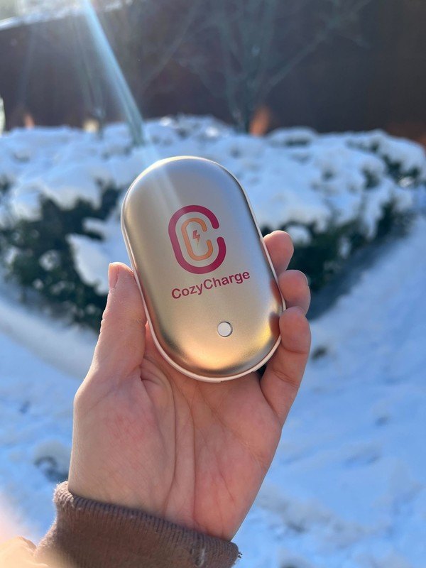 A hand holding the pocket-size CozyCharge rechargeable hand warmer outdoors
