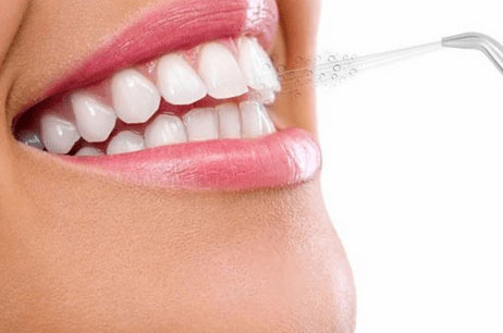 Person using a water flosser tip along the gumline of their teeth