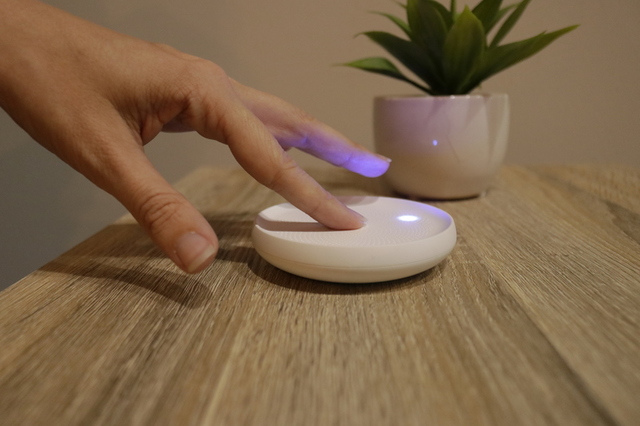 Finger tapping the Dodow on a nightstand to start a session, blue light glowing