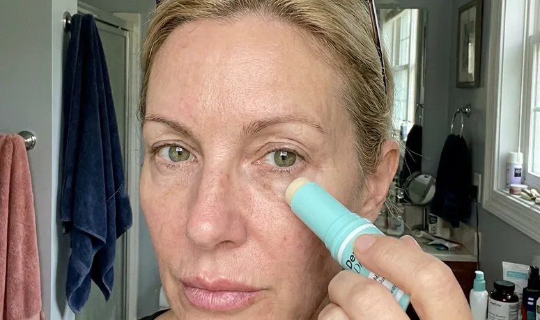 A woman in a bathroom swiping the Dr. Melasmin balm stick along the skin under her eye