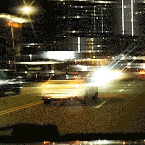 A glare-filled night driving scene of oncoming headlights and city lights on a highway