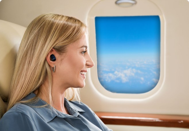 A traveler wearing a black Echo Labs earbud on a plane while looking out the cabin window