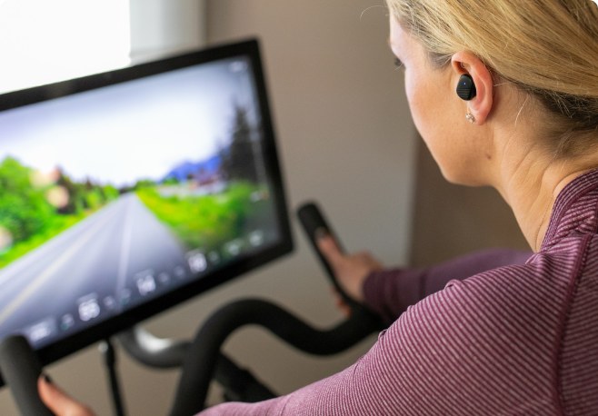 A person wearing a black Echo Labs earbud during an indoor cycling workout
