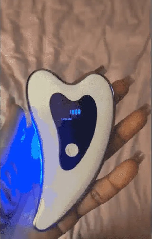 The Glokore electric gua sha held in a hand showing its lit massage-mode display