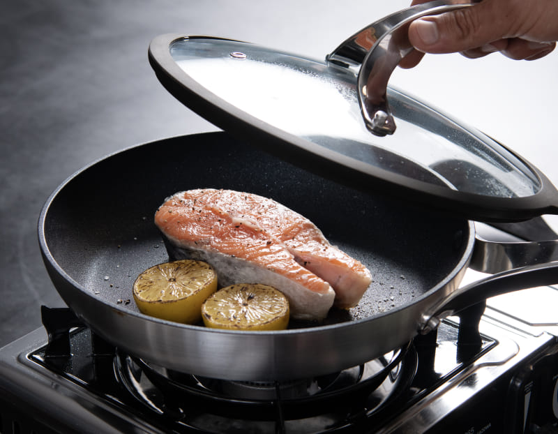 Salmon and lemon searing in the Emura non-stick pan on a gas burner with the lid lifted