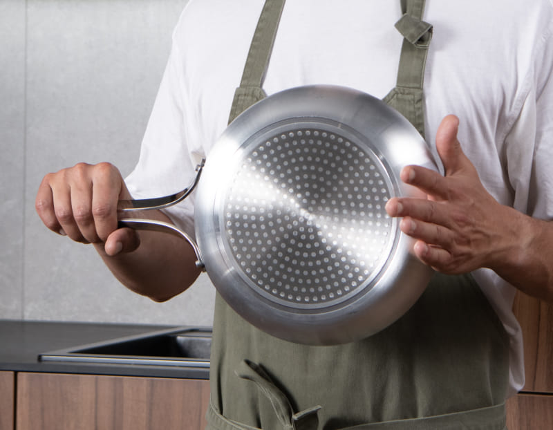 Underside of the Emura frying pan showing the dimpled stainless base and riveted handle