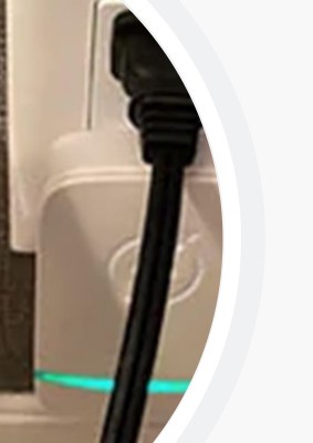 The white StopWatt energy saver plugged into a wall outlet next to an appliance cord, with its green indicator light lit