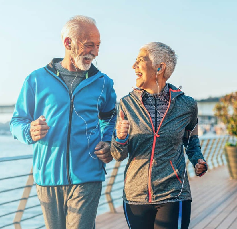 An active older couple jogging along a waterfront, the everyday fitness routine a smart body-composition scale like the FitScale X is built to track
