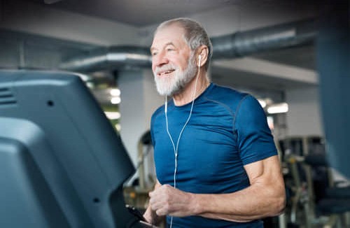 A man smiling on a treadmill with earbuds in, the kind of regular routine a body-composition scale like the FitScale X is meant to track