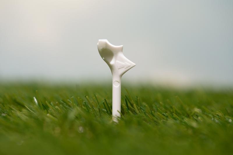 A white FlightPath golf tee standing in the grass on a tee box