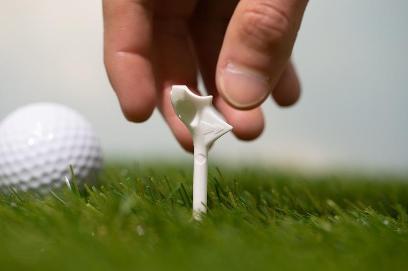 A hand placing a FlightPath golf tee into the ground next to a golf ball
