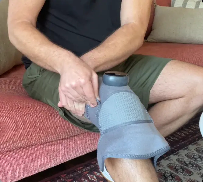 Man sitting on a couch wearing the Glokore Knee Massager on his knee