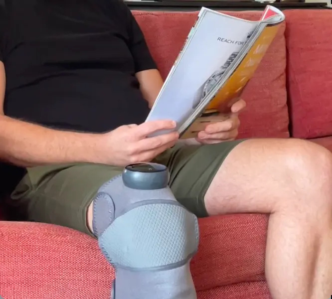 Man relaxing on a couch reading while wearing the Glokore Knee Massager