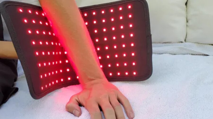 Forearm resting on the Glokore Red Light Therapy Wrap with the LEDs glowing red