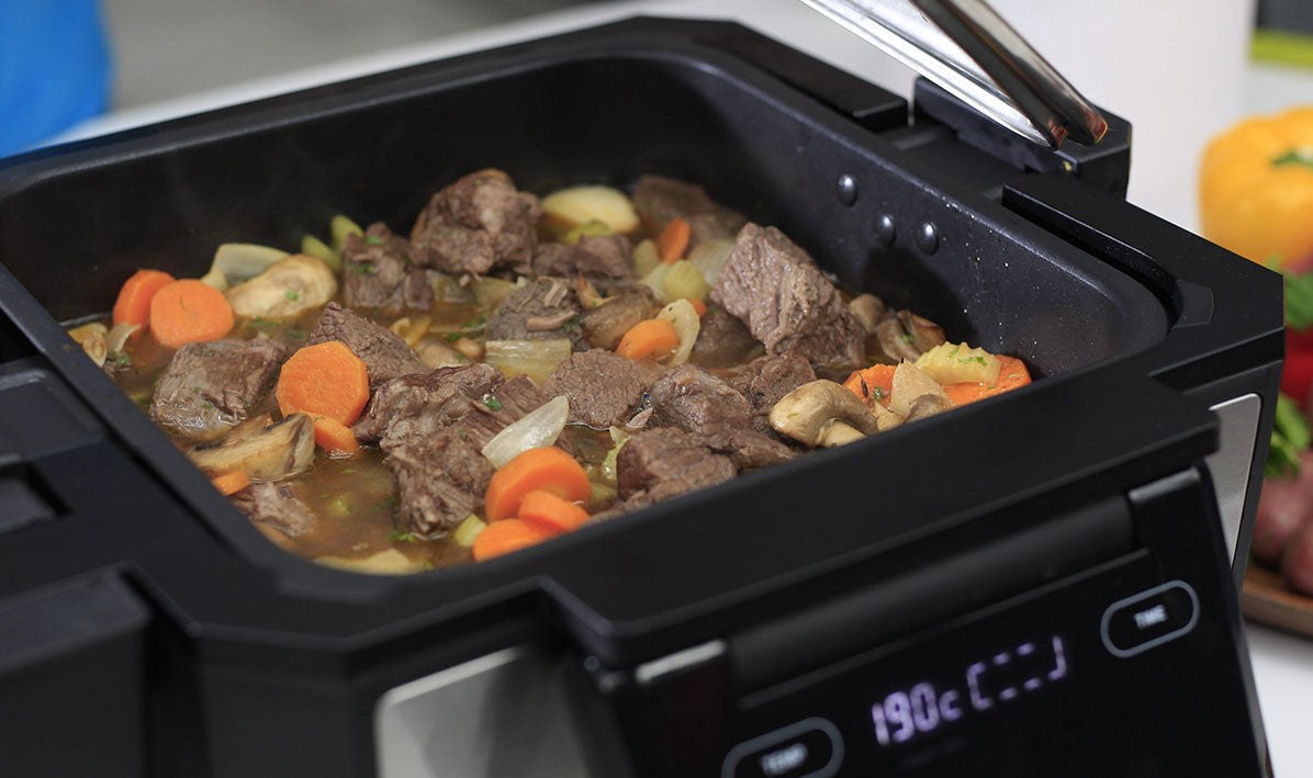 A beef and vegetable stew slow cooking in the Gourmax Pro's deep tray with the temperature display lit