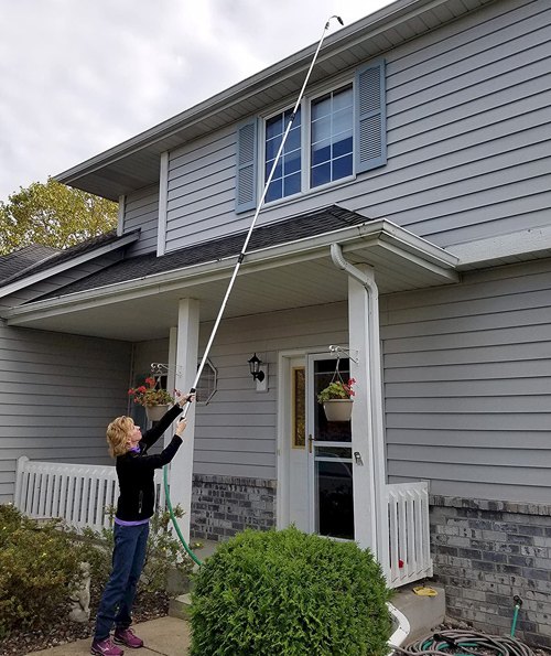 Gutter Hero telescopic wand extended up to a two-story roofline gutter while the user stands on the ground