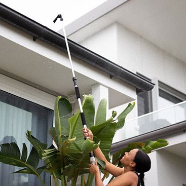 A person using the Gutter Hero telescopic wand to rinse leaves from a house gutter without a ladder