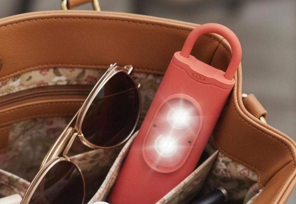 Coral Halo Siren personal safety alarm tucked inside a handbag next to sunglasses, strobe lit