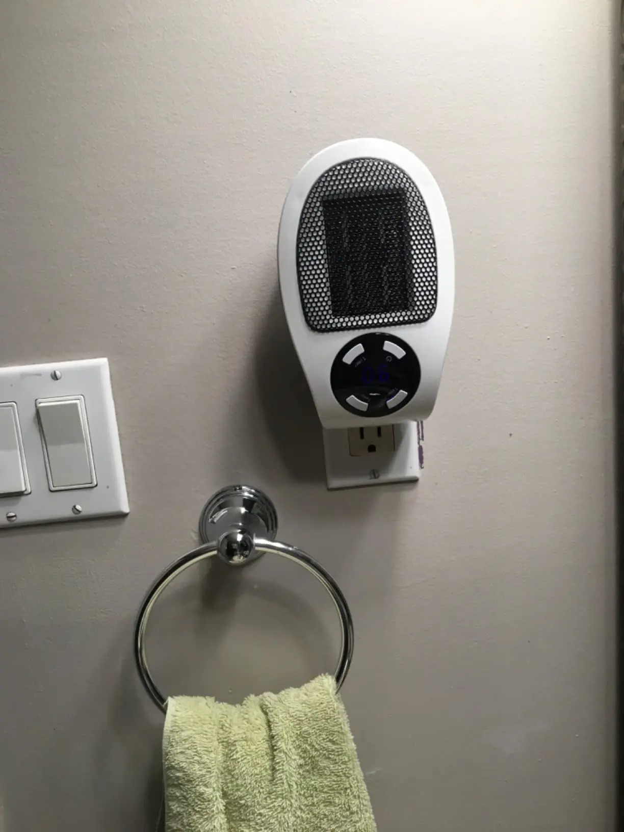 Heat Space plug-in heater running in a bathroom, plugged into a wall outlet above a towel ring