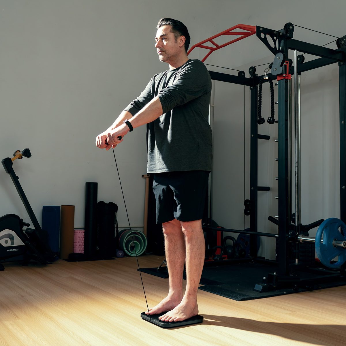 A person standing barefoot on the Herz P1 Smart Scale and holding its retractable handle to run a full-body measurement in a home gym